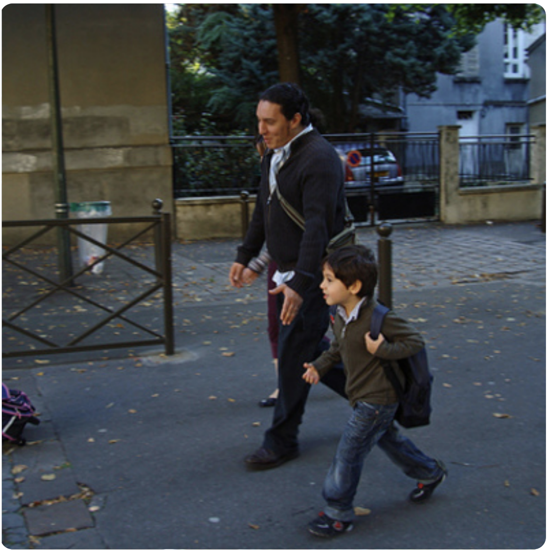 Es un hombre y un niño caminando por la acera. El hombre parece que va a trabajar y el niño va a la escuela.
